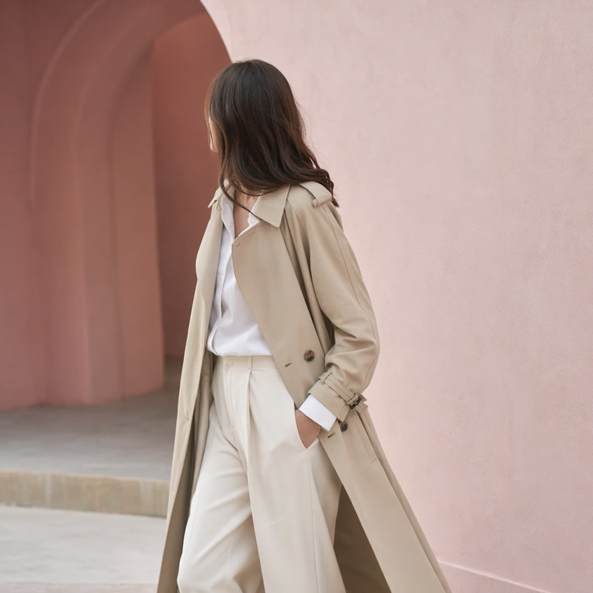 A woman wearing a classic trench coat over a white shirt and trousers — a timeless essential layer